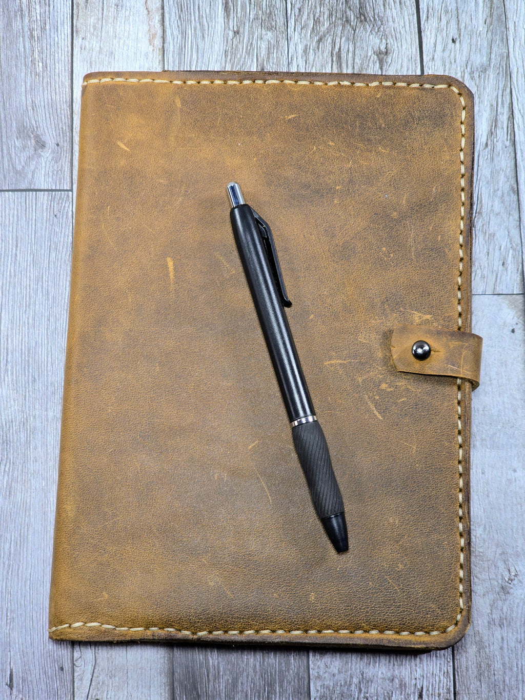 Brown leather journal cover with a pen on a wooden surface 
