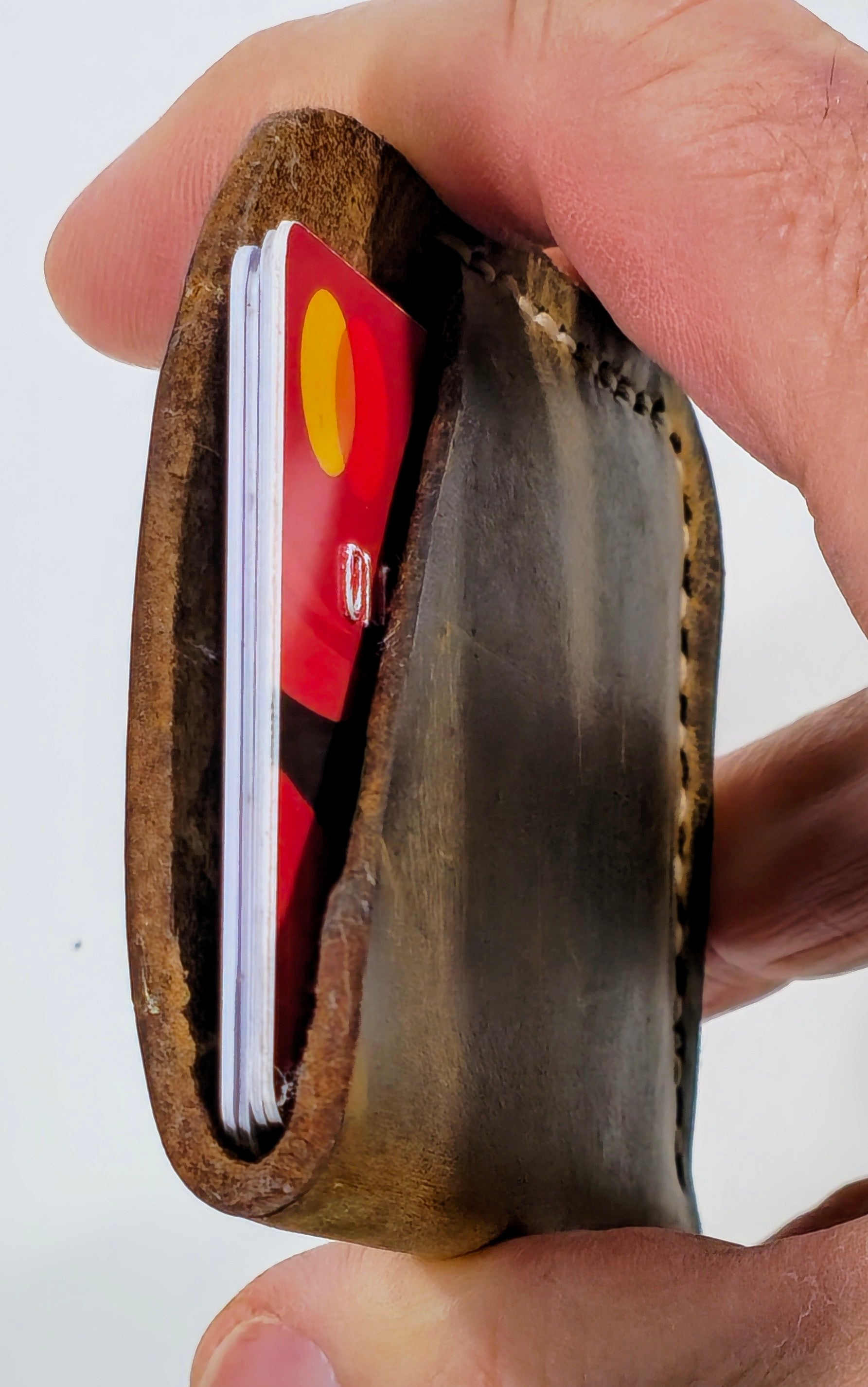 Hand holding a small leather wallet with a card inside on a white background