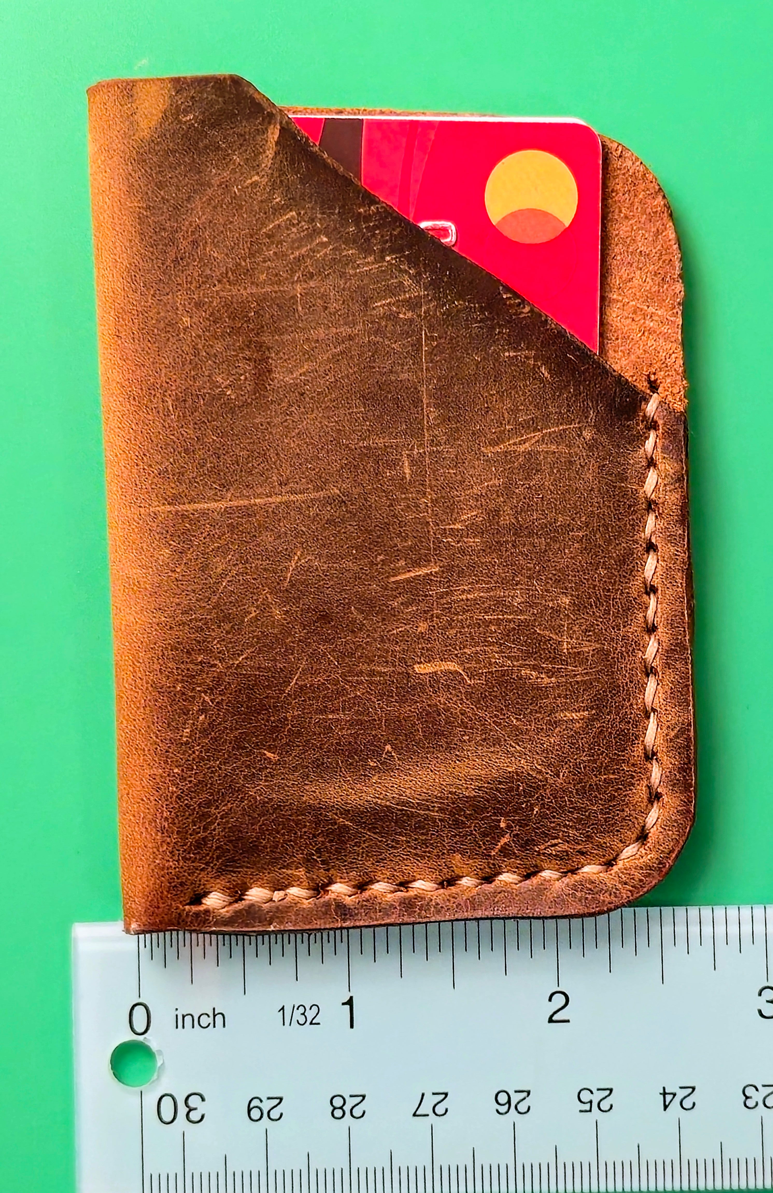 Brown leather wallet with a red card on a green background, next to a ruler for size reference.