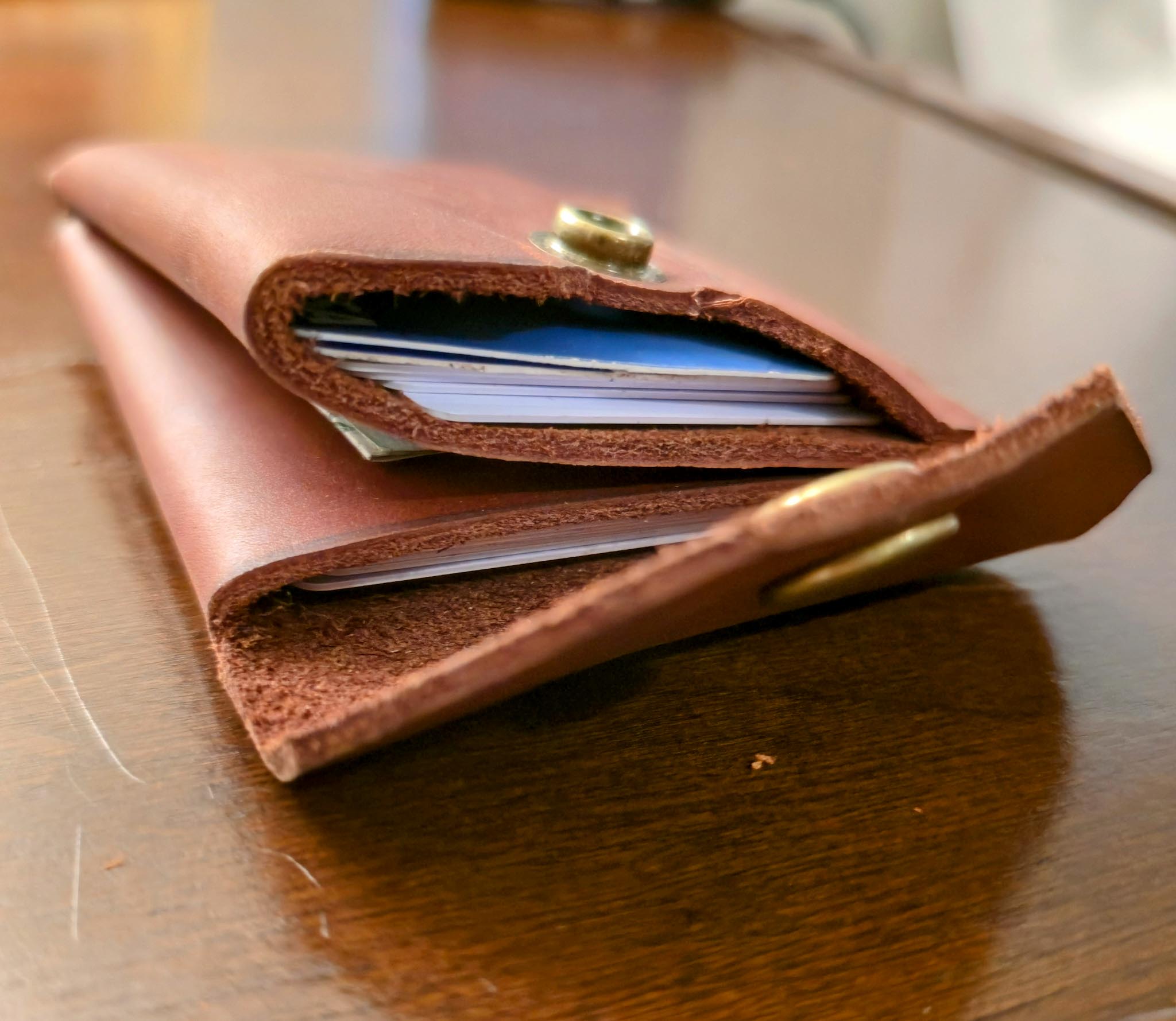 Burgundy leather wallet with an antique brass snap accents on a wooden surface