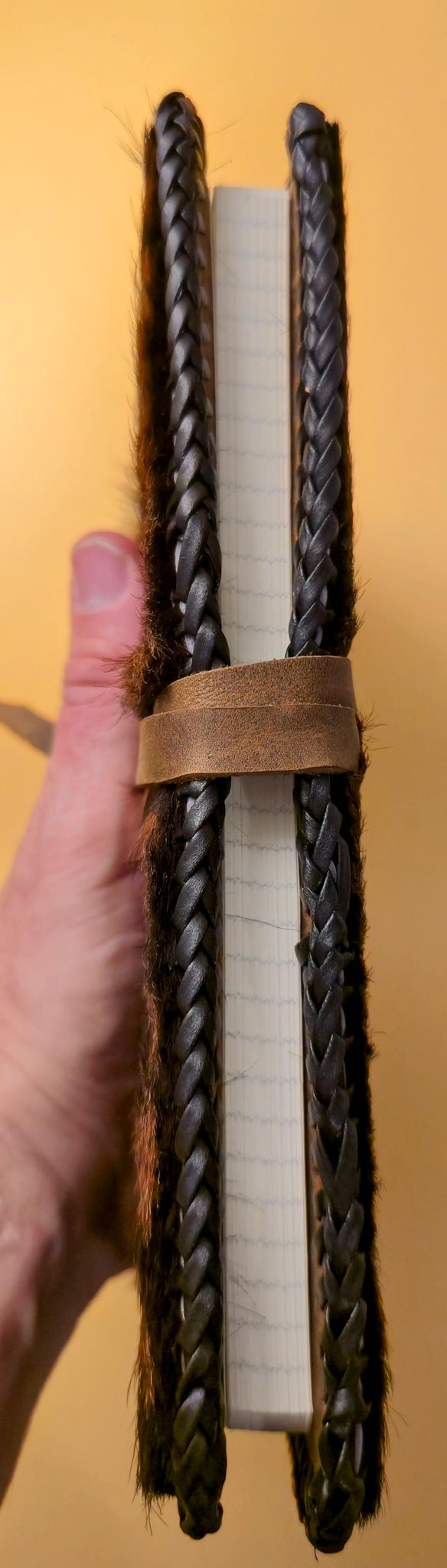 Vertical side view of Hair on leather journal cover - Luxury handmade leather notebook protector being held by a hand