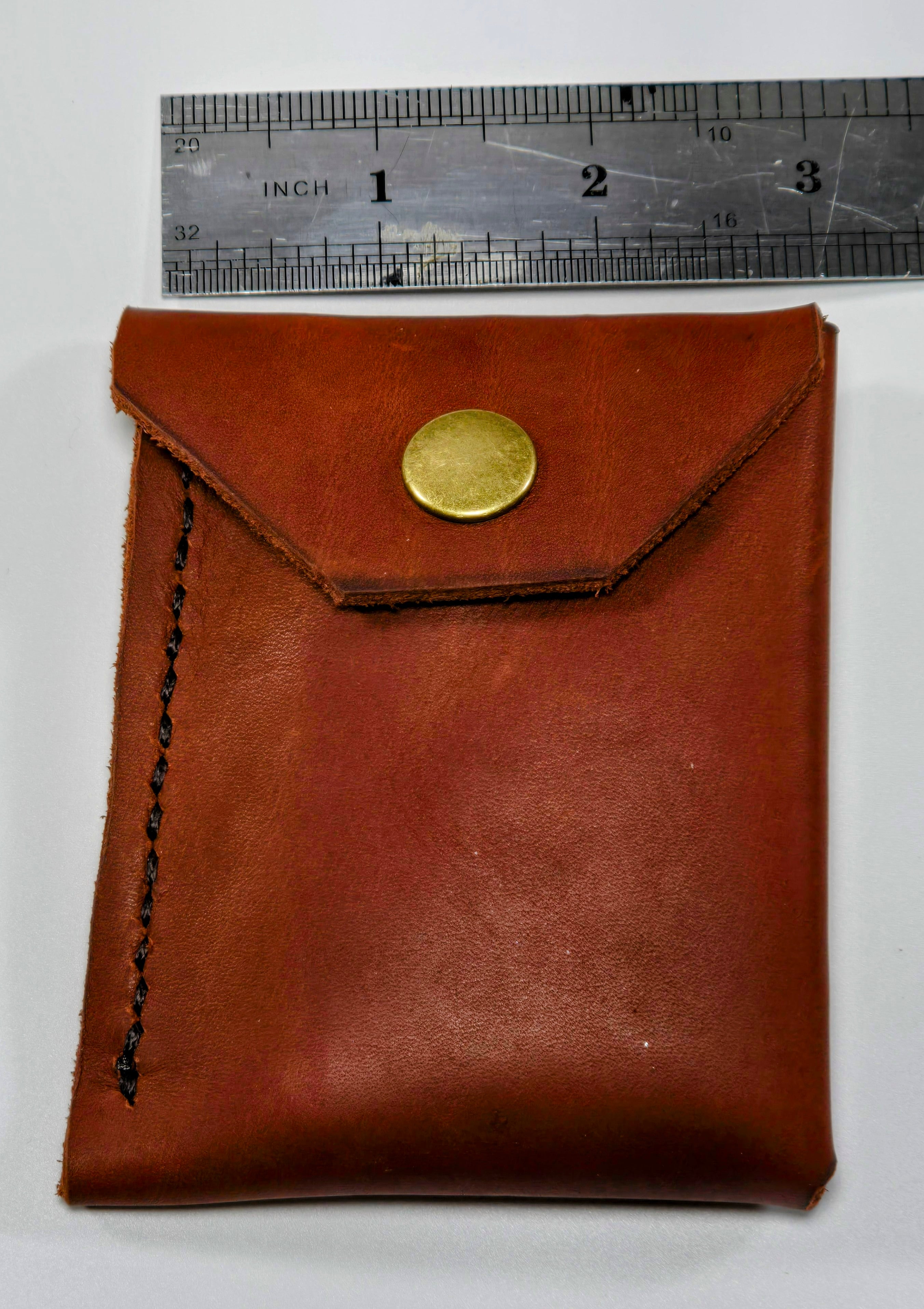Burgundy leather minimalist wallet with a antique brass snap next to a ruler for scale
