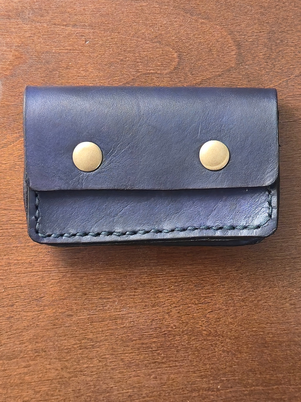 Blue leather card wallet with brass magnetic snaps but on a wooden surface