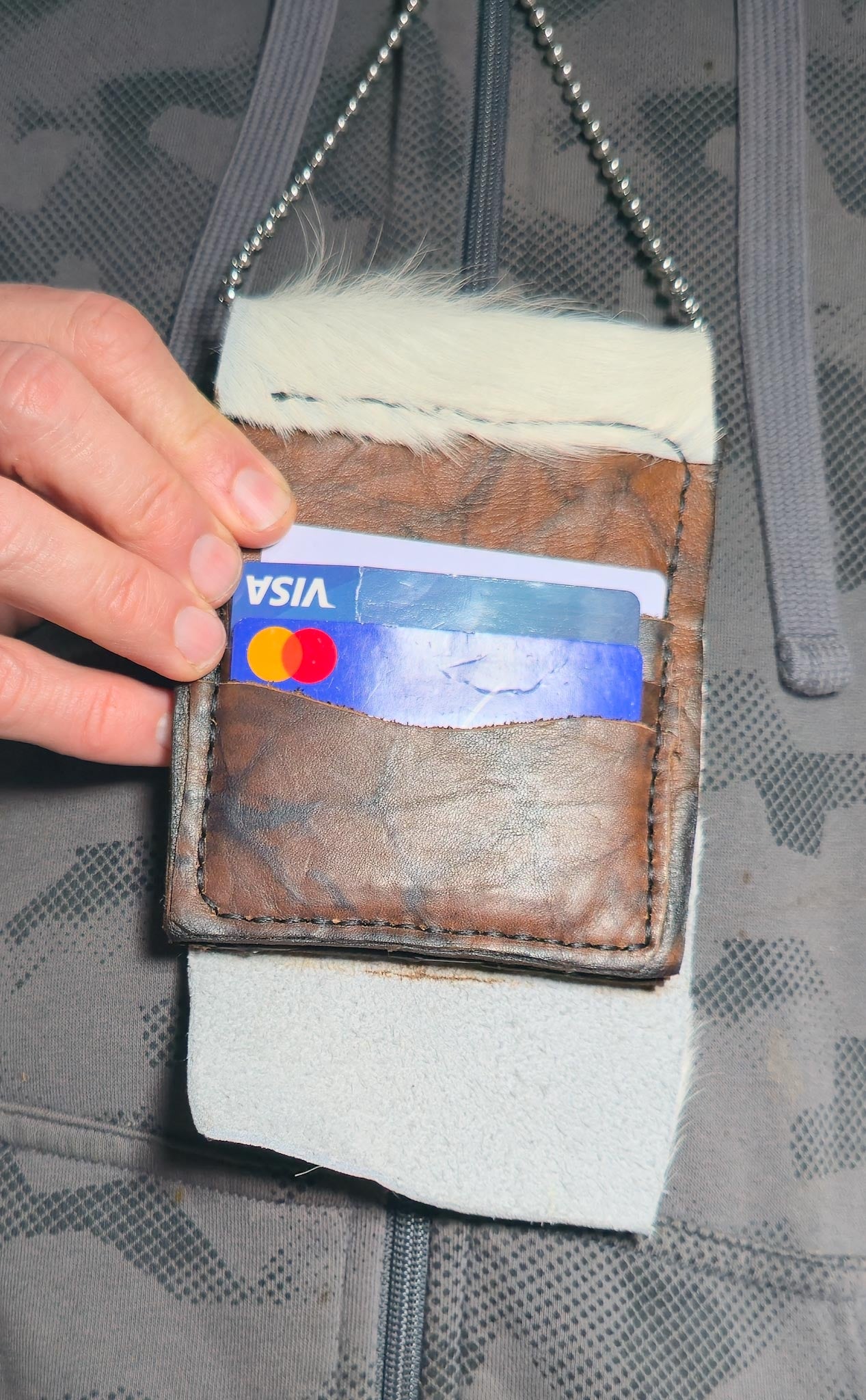 Hand holding a Visa card over a leather wallet with a textured background