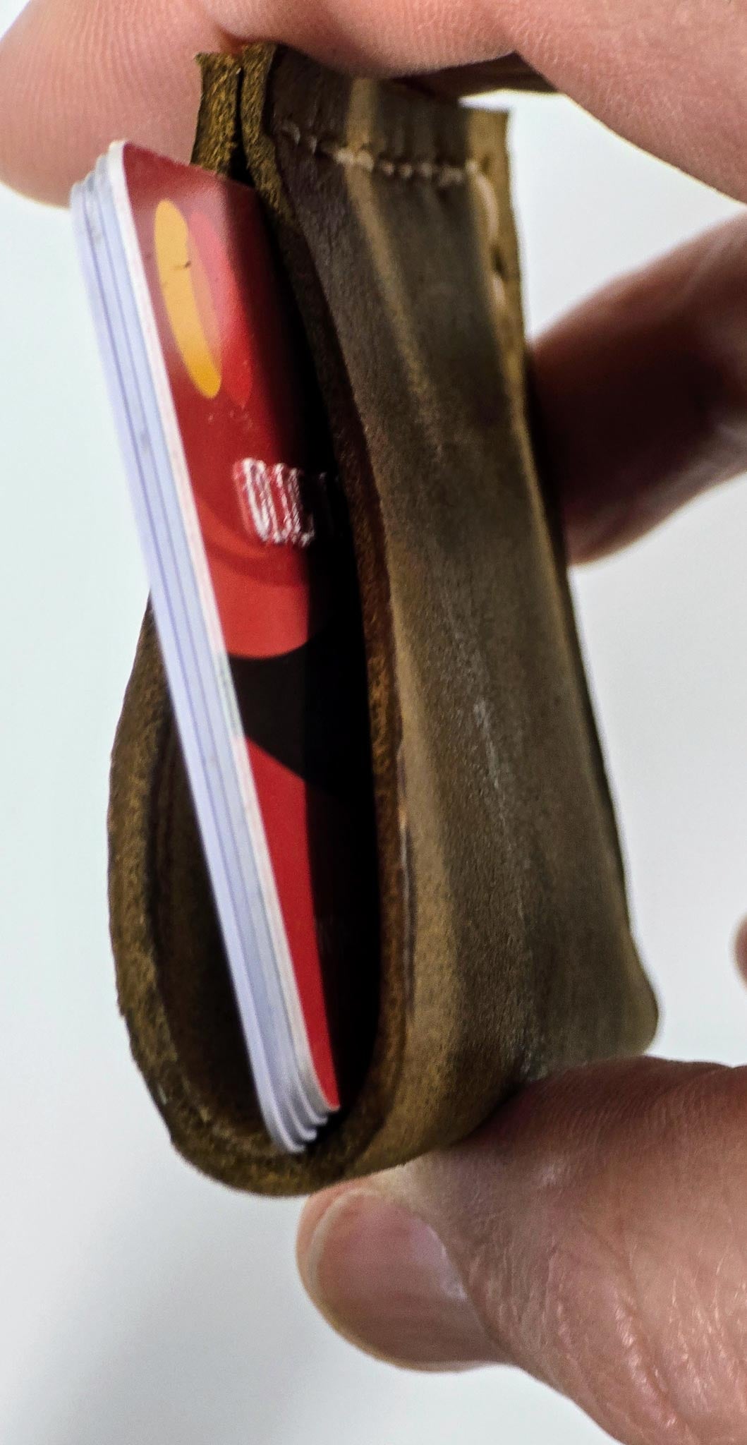Hand holding a brown leather wallet with a red card inside on a white background