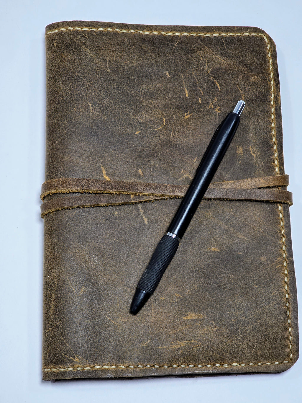 Brown leather mini padfolio with a black pen on a light blue background