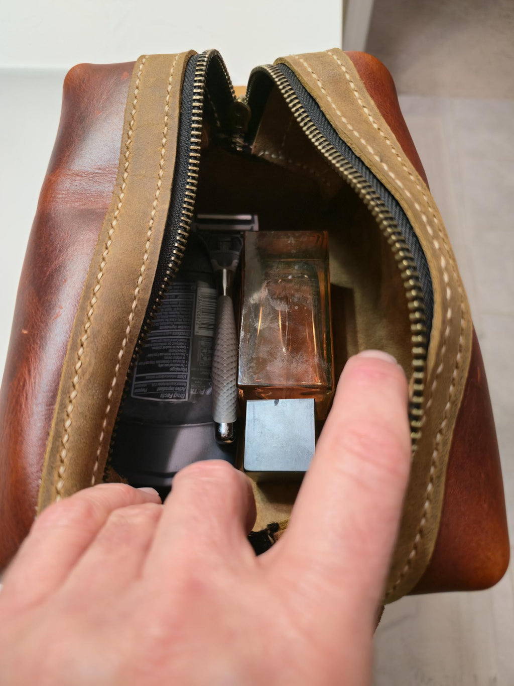 Burgundy leather toiletry bag with grooming items inside, held open by a hand.