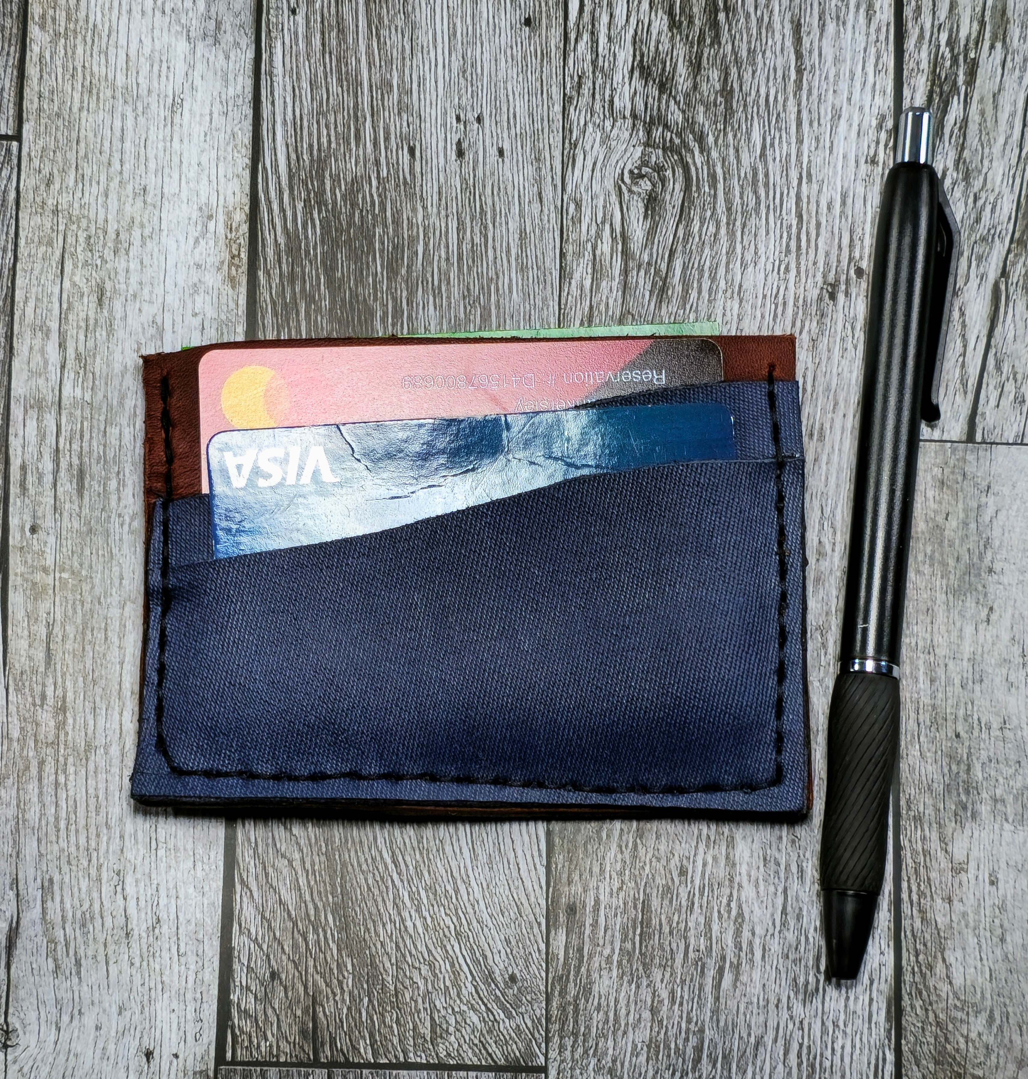 Navy blue cardholder with cards on a wooden surface next to a black pen