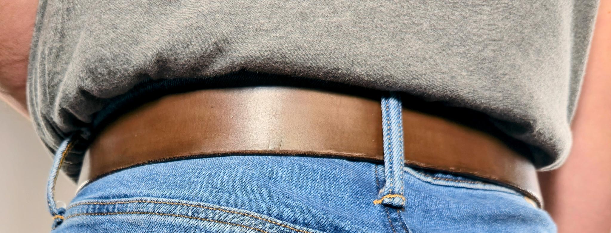 Person wearing a gray sleeveless top and blue jeans with a chocolate brown belt.