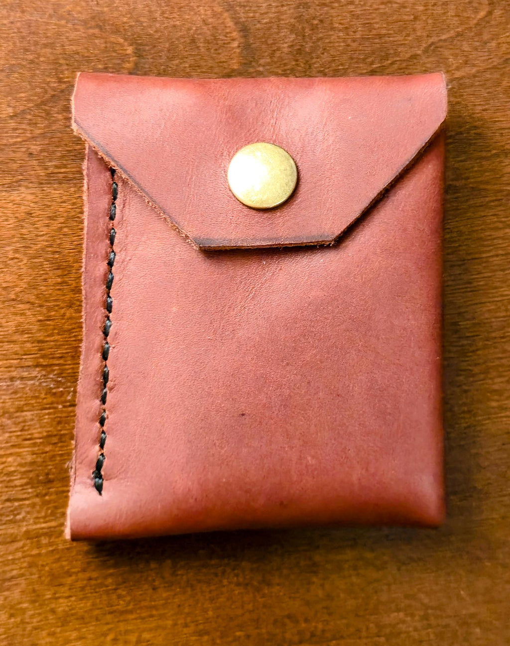 Burgundy leather minimalist wallet with an antique brass snap on a wooden surface