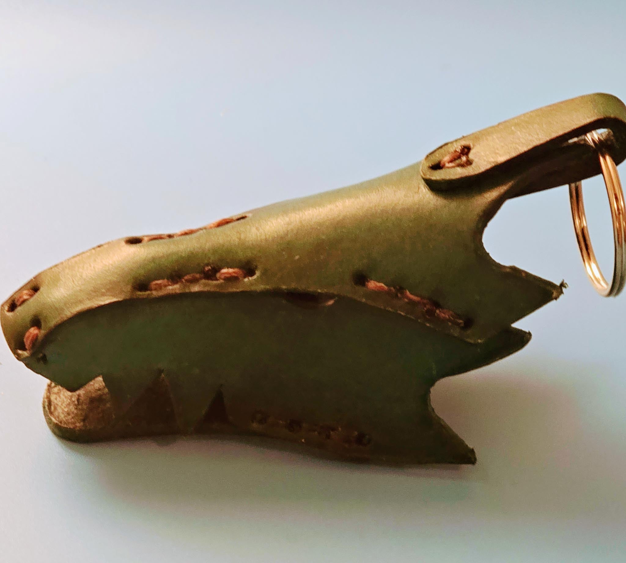 Close-up of a handmade leather dragon key fob showing intricate scale texture and rustic green finish.