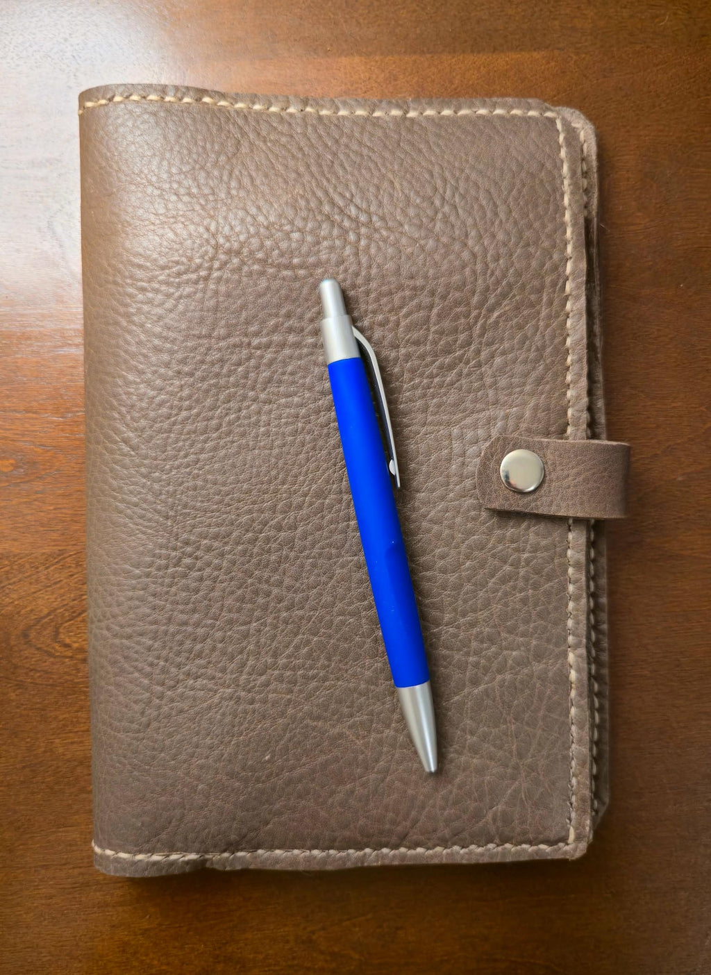 Brown leather mini padfolio with a blue pen on a wooden surface