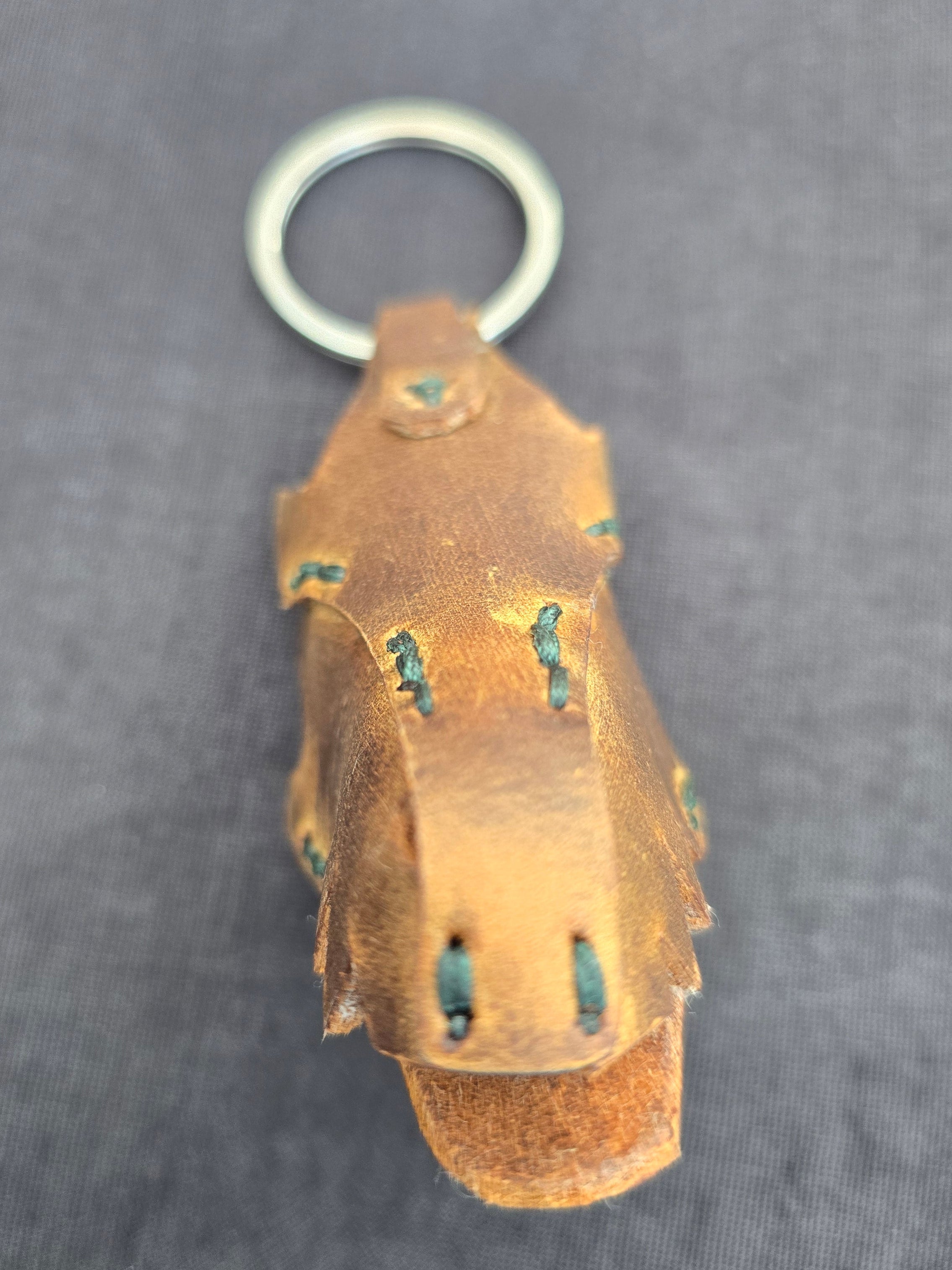 Brown-colored leather dragon keychain with a metal ring on a dark gray background
