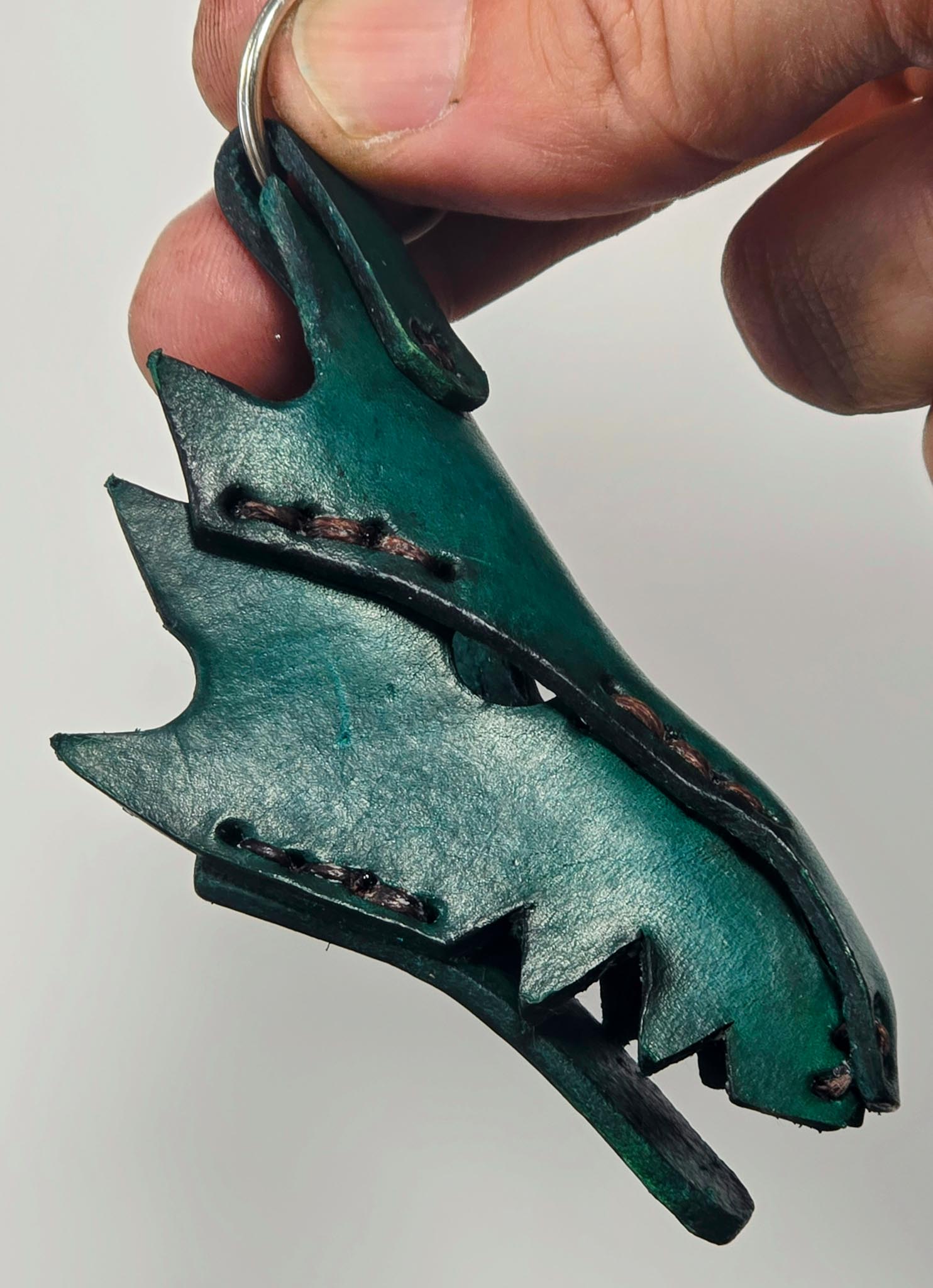 Close-up of a handmade leather dragon key fob showing intricate scale texture and rustic green finish.