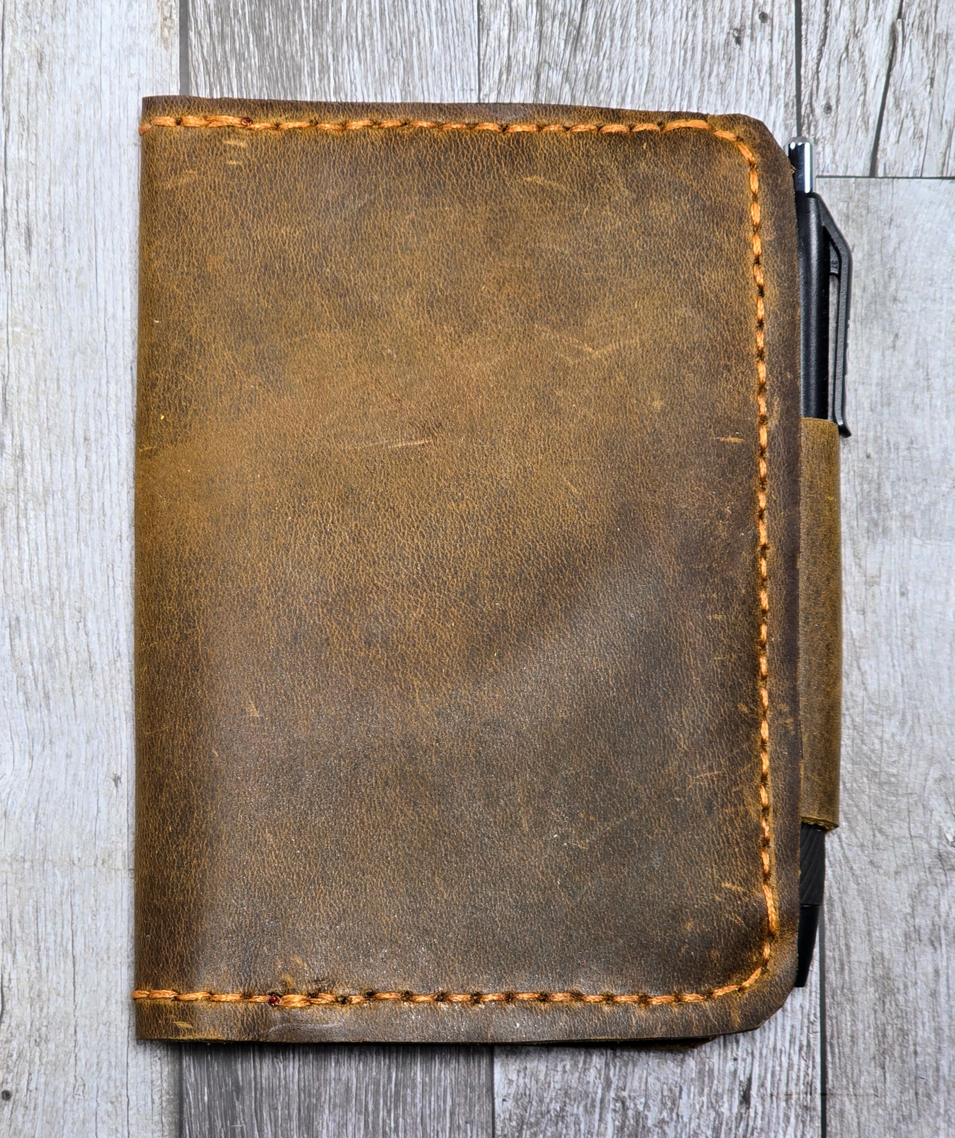 Brown leather notebook with pen holder on a wooden surface