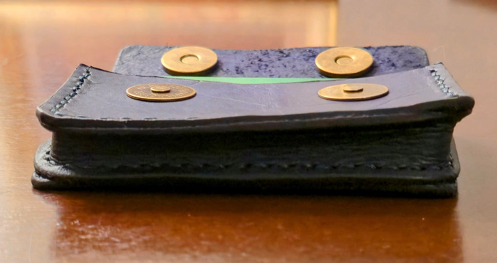 Navy blue leather card wallet with brass magnetic snaps, side view on a wooden surface