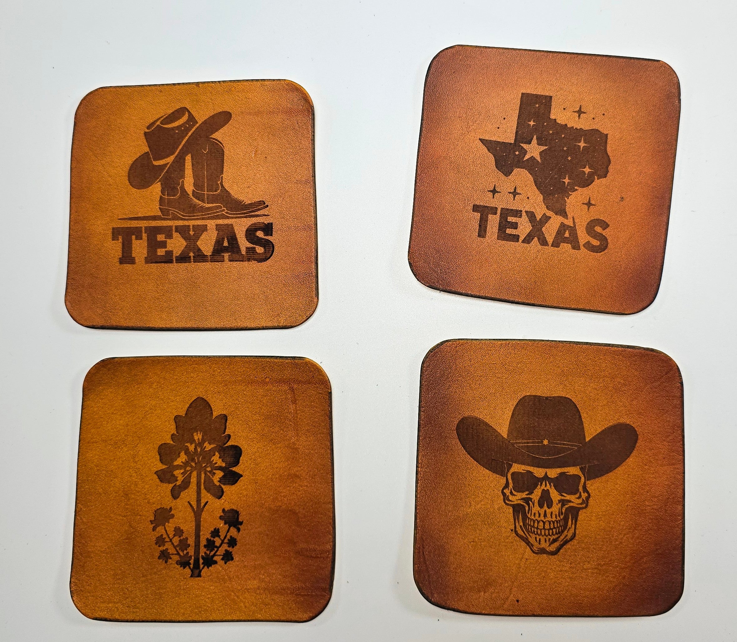 Four leather coasters with Texas-themed designs on a white background