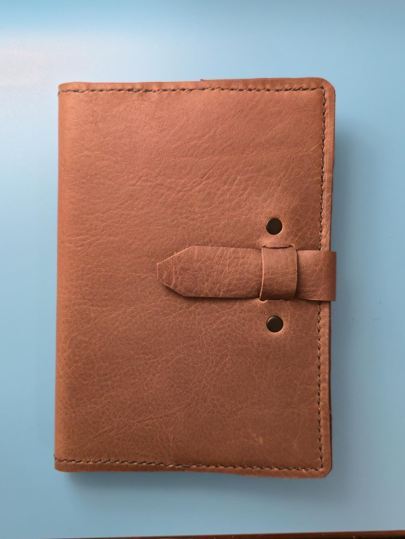 Brown leather notebook with a strap on a light blue background