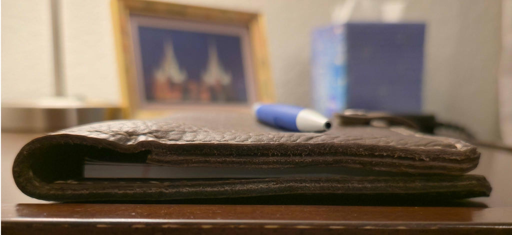 Side view of Brown embossed leather mini padfolio on a wooden surface with a blurred background