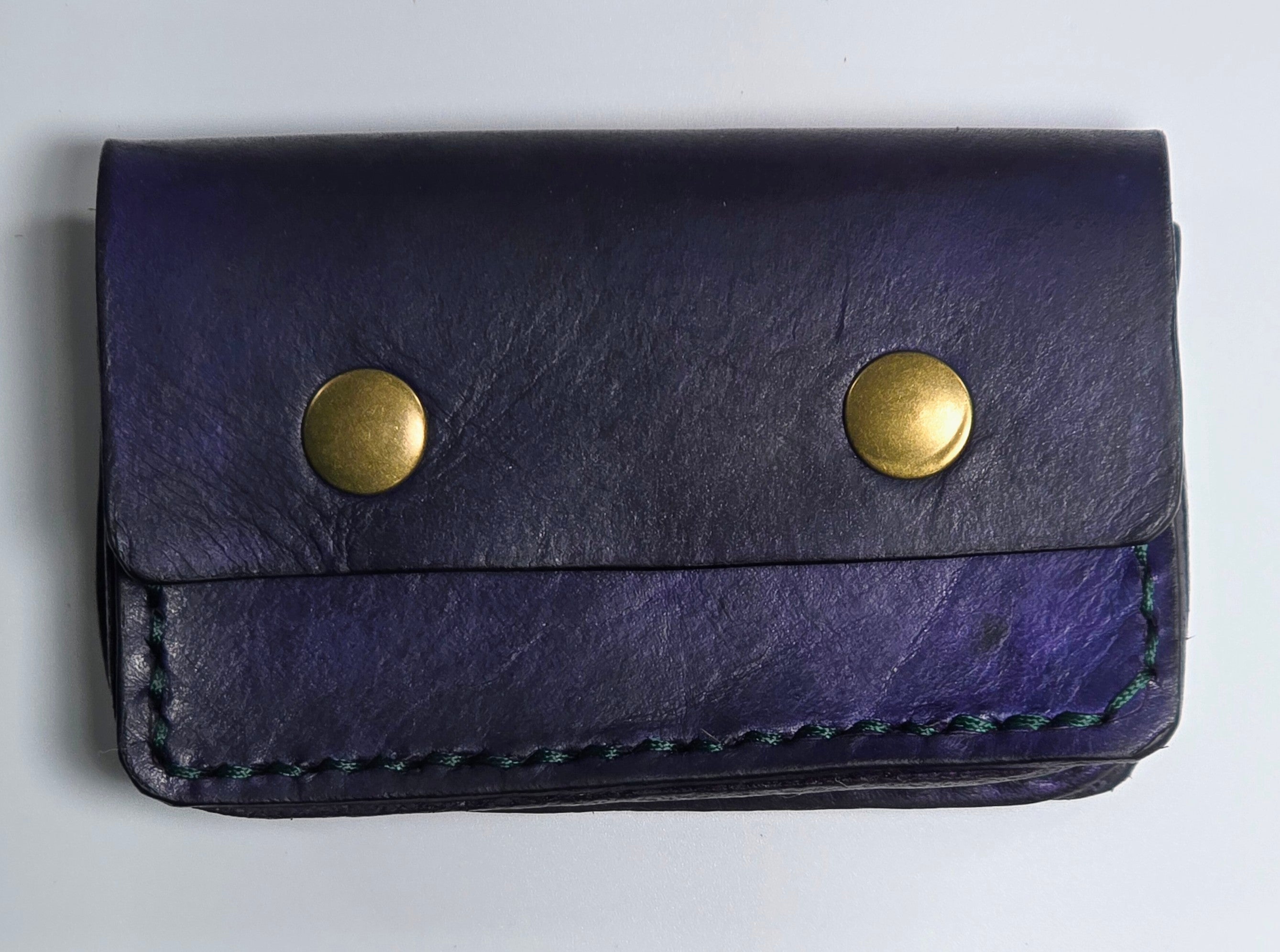 Navy leather card wallet with brass magnetic snaps on a light gray background