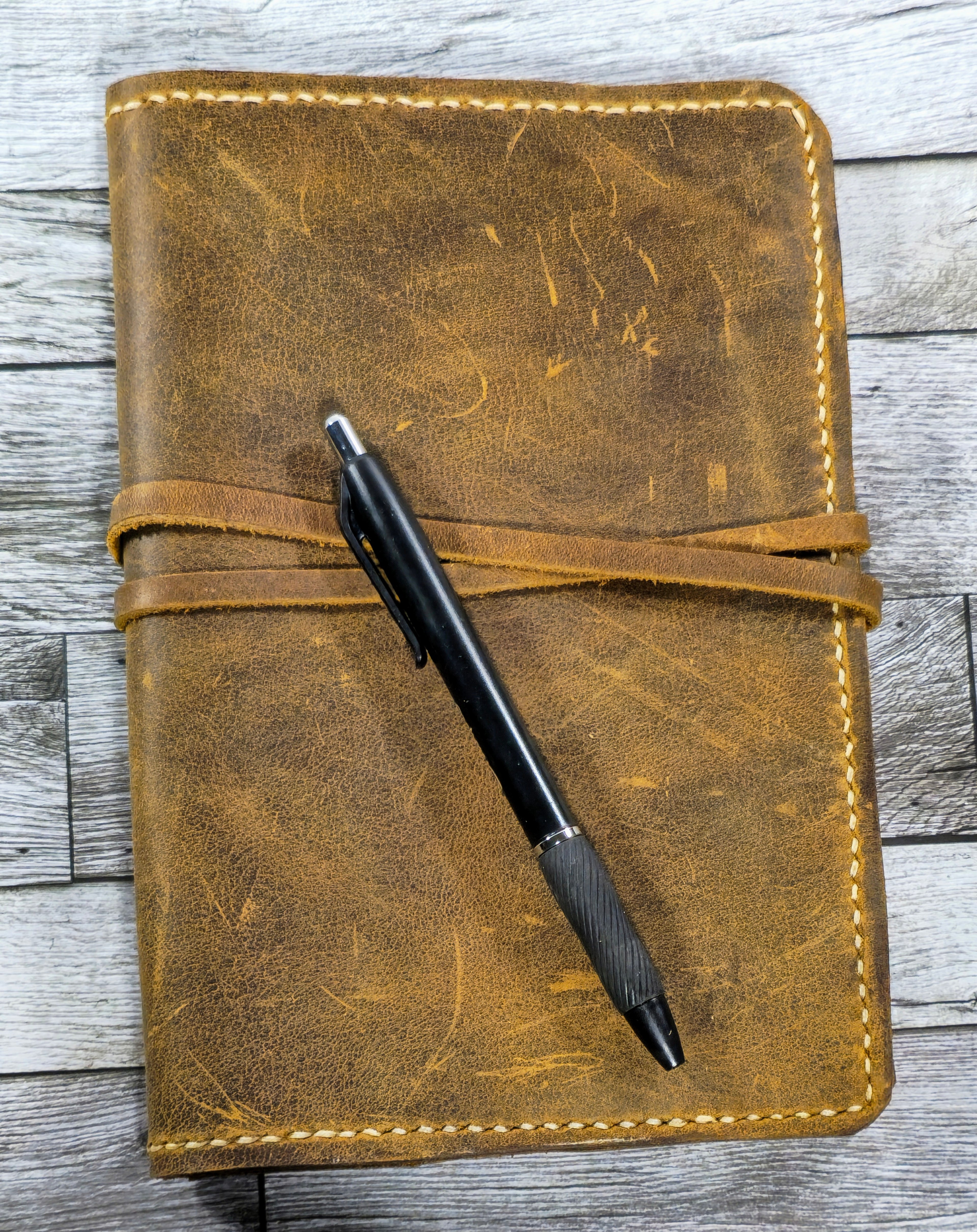 Brown leather notebook with a black pen on a wooden surface