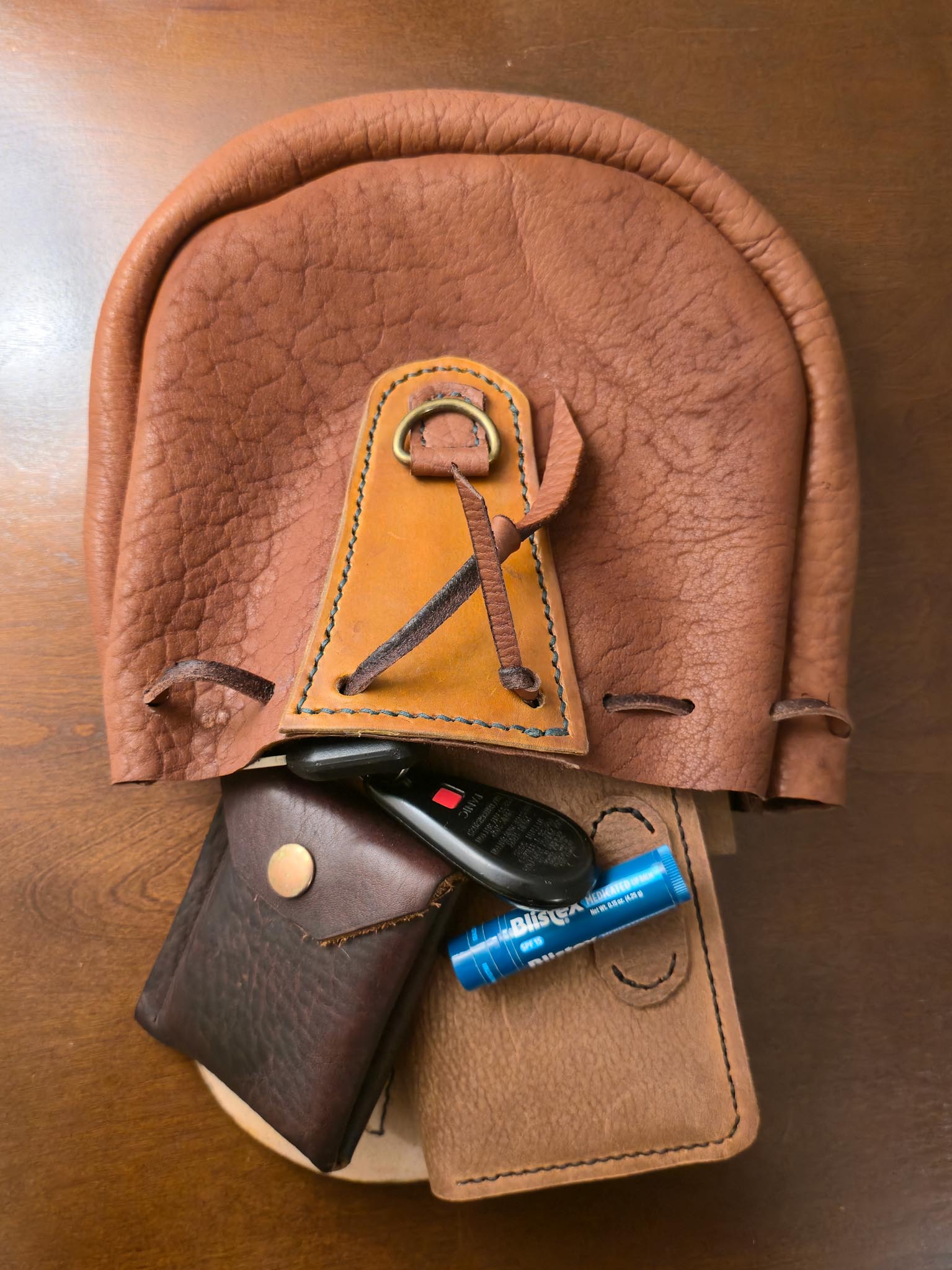 Tan buffalo leather pouch with various items on a wooden surface