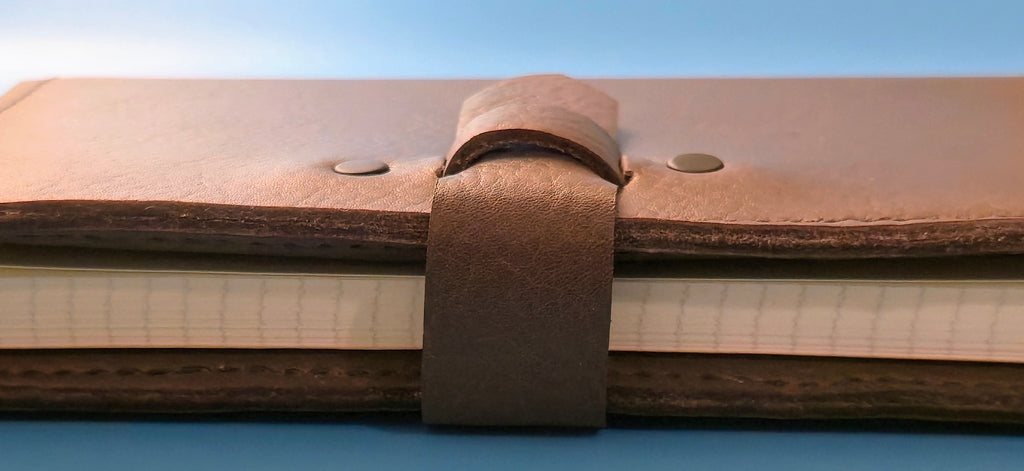 Close-up of a side view of brown embossed leather journal cover with a strap closure on a blue background