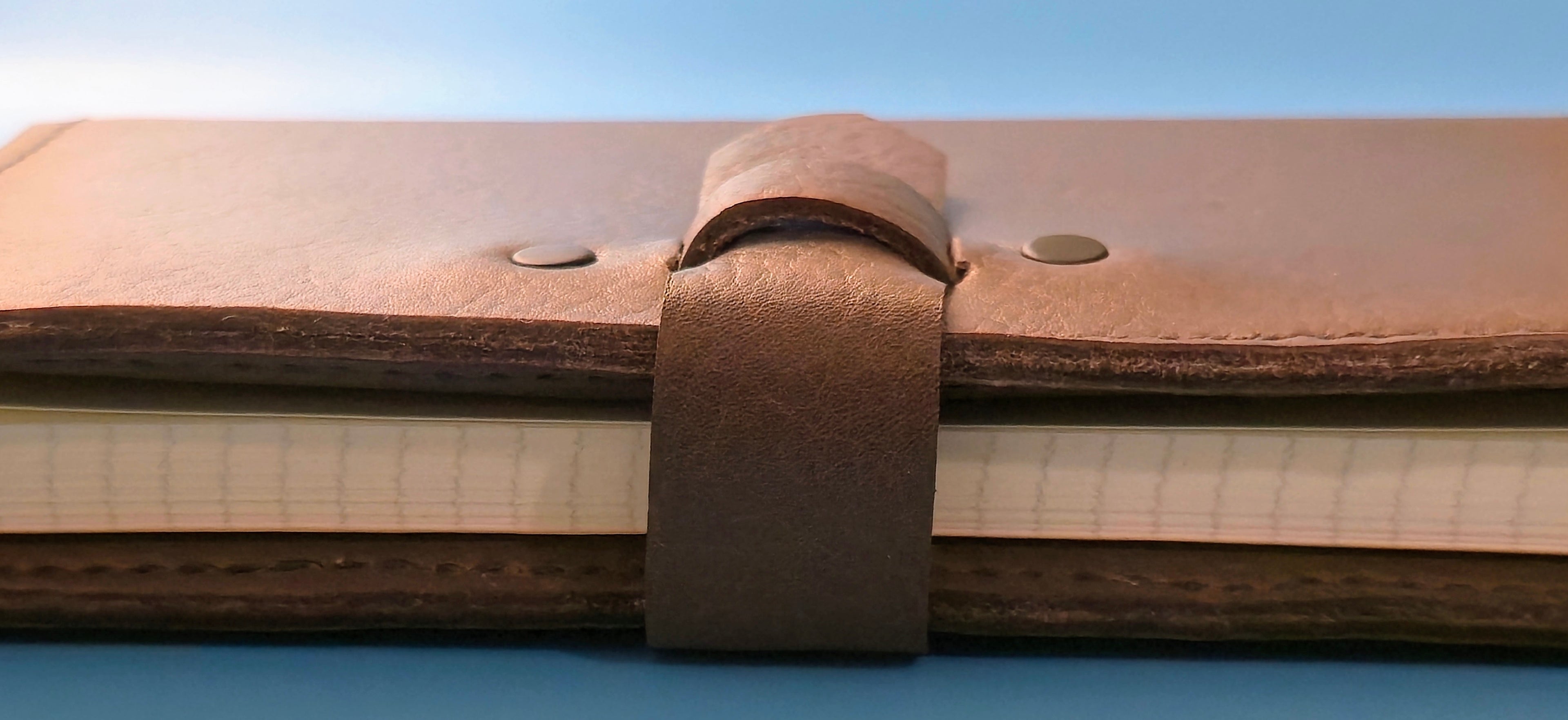 Close-up of a brown leather-bound notebook with a strap closure on a blue background