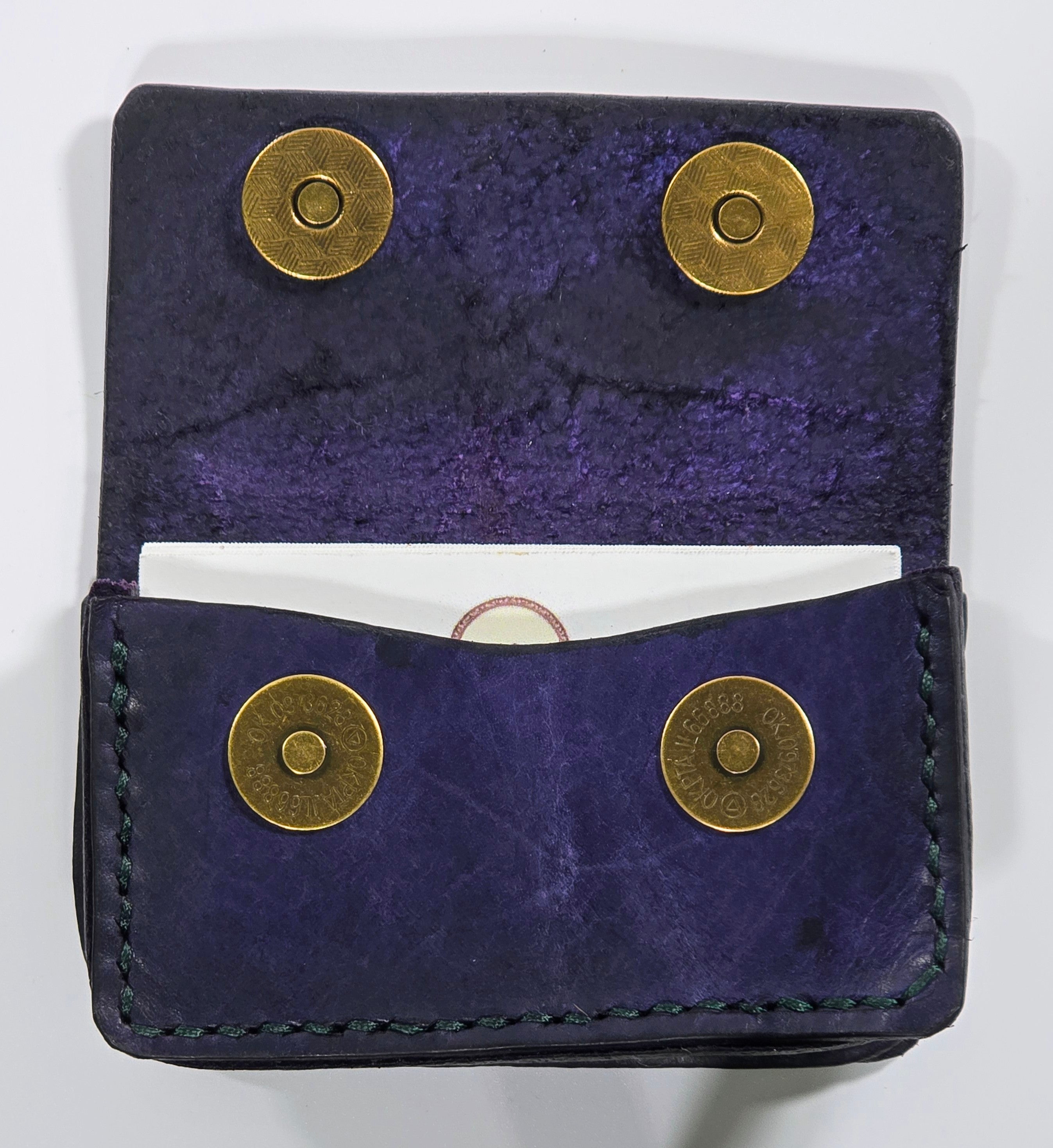 Navy blue leather card wallet with brass magnetic snaps on a white background, open with cards inside