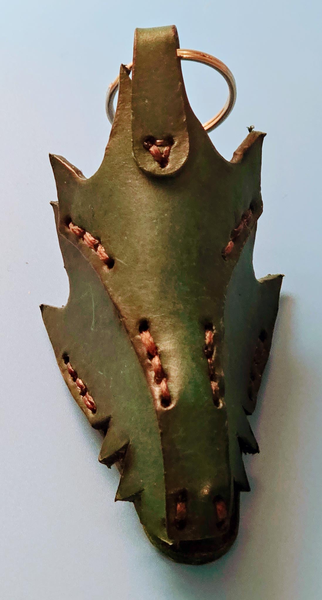 Close-up of a handmade leather dragon key fob showing intricate scale texture and rustic green finish.