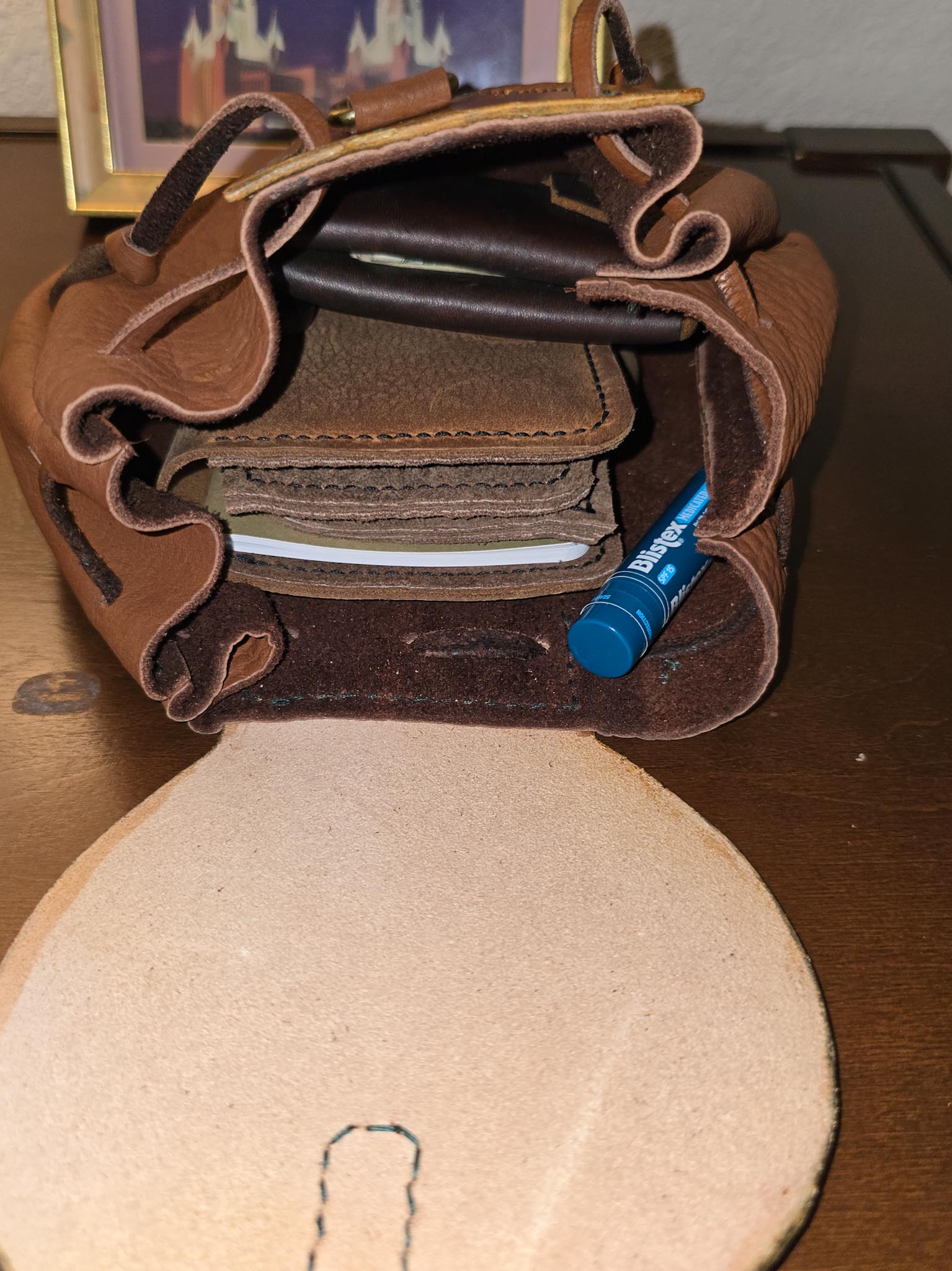 Inside of tan buffalo leather belt pouch with wallet, keys, journal, and lip balm on wood surface.