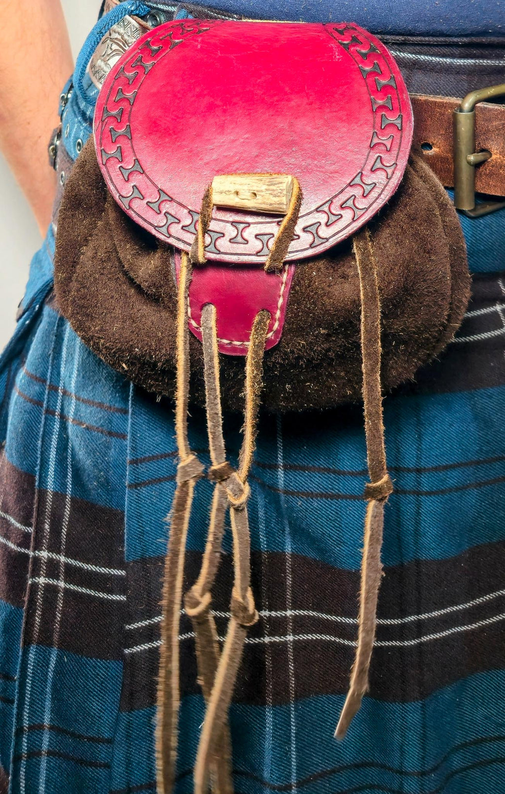 A leather sporran belt pouch worn on a kilt, showing its slim profile and secure belt loops for hands-free carry.